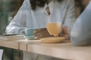 Two people enjoying coffee in a café with a serene ambiance, viewed through a window.